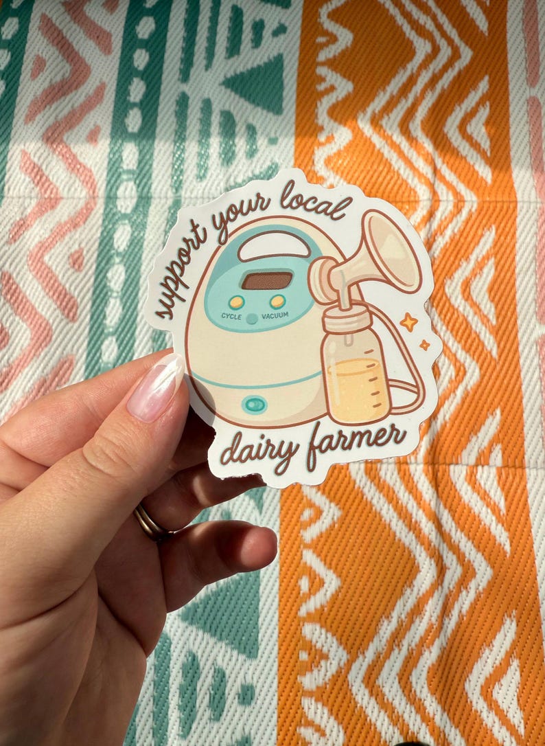 May include: A sticker depicting a breast pump and a bottle of milk, with the text "support your local dairy farmer". The design is a cartoon style. The background is a patterned fabric in various colours.