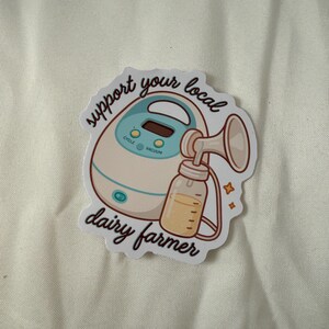 May include: A sticker showing a breast pump and a bottle of milk. The text on the sticker reads "support your local dairy farmer". The pump is white and teal, and the bottle is clear with yellow liquid.