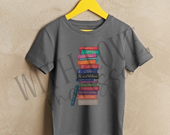 May include: A dark grey t-shirt featuring a stack of colourful books printed on the front. The books have titles such as "A Court of Thorns and Roses" and "The Cruel Prince".
