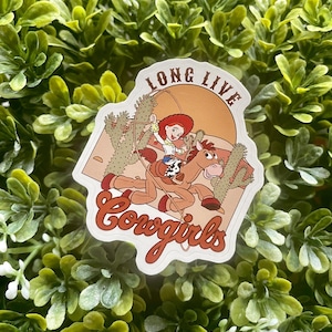 May include: A white sticker with a cartoon image of a cowgirl riding a horse with the text "Long Live Cowgirls" in a brown and orange color scheme.