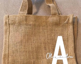 May include: A brown burlap tote bag with a white letter "A" and the text "Alexandra" in cursive on the front.