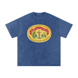 May include: Blue t-shirt featuring a Grateful Dead logo with an anchor, botanical elements, and text that reads "The music never stopped" and "Made in San Francisco since 1965". The logo is in a yellow oval.