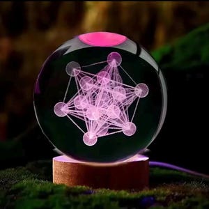 May include: A clear glass sphere with a pink geometric design inside, illuminated by a pink light. The sphere sits on a wooden base, with a dark background.