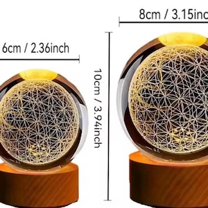 May include: Two spherical glass lamps with an internal laser-etched flower of life pattern, illuminated by warm light. The smaller lamp is 2.36 inches wide and 3.15 inches tall. The larger lamp is 3.15 inches wide and 3.94 inches tall on wooden bases.