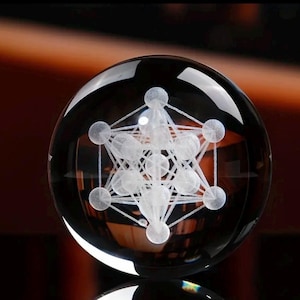 May include: A clear glass sphere featuring an internal laser-etched white geometric pattern known as Metatron's Cube. The design consists of multiple interconnected spheres and straight lines, creating a complex three-dimensional structure.