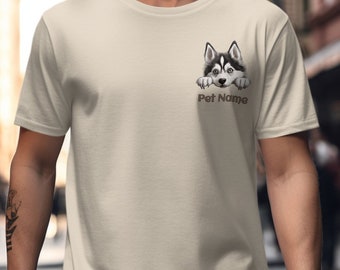 Op de afbeelding: Een beige t-shirt met korte mouwen voorzien van een afbeelding van een zwart-witte husky-pup die boven de tekst Pet Name uitsteekt, gedrukt in een bruin schreefloos lettertype op de linkerborst van het kledingstuk.