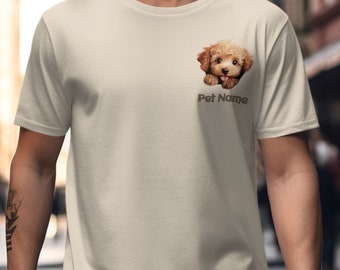 May include: A beige short-sleeved t-shirt featuring a graphic of a small, fluffy, light brown puppy peeking out from the upper left chest area. Below the puppy graphic, the text Pet Name is printed in a dark brown, sans-serif font.