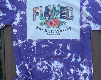 May include: Purple tie-dye t-shirt with a white square graphic that says "Flawed But Still Worthy Romans 5:8" with floral accents.
