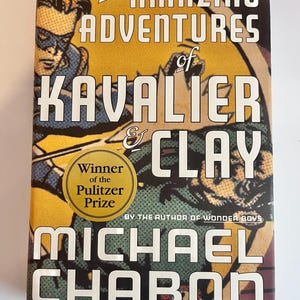 May include: A hardcover book titled "The Amazing Adventures of Kavalier & Clay" by Michael Chabon. The cover features a comic book style illustration with a superhero figure and the text "Winner of the Pulitzer Prize".
