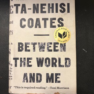 May include: A book cover for "Between the World and Me" by Ta-Nehisi Coates. The cover is off-white with black text, including the title and author's name. A gold sticker indicates a National Book Award winner. The book is a New York Times bestseller.