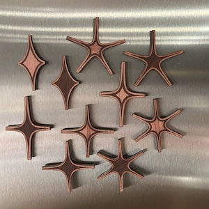 May include: Nine wooden star-shaped coasters in shades of brown. The coasters have a geometric design and are arranged in a cluster on a silver surface.