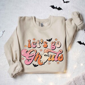 May include: A beige sweatshirt with a pink and orange graphic that says "Let's go Ghouls" with a ghost and stars.