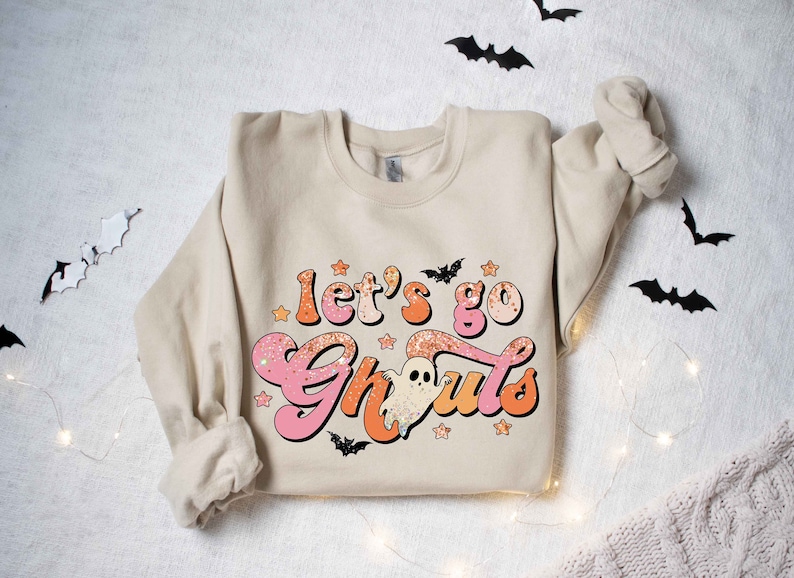 May include: A beige sweatshirt with a pink and orange graphic that says "Let's go Ghouls" with a ghost and stars.