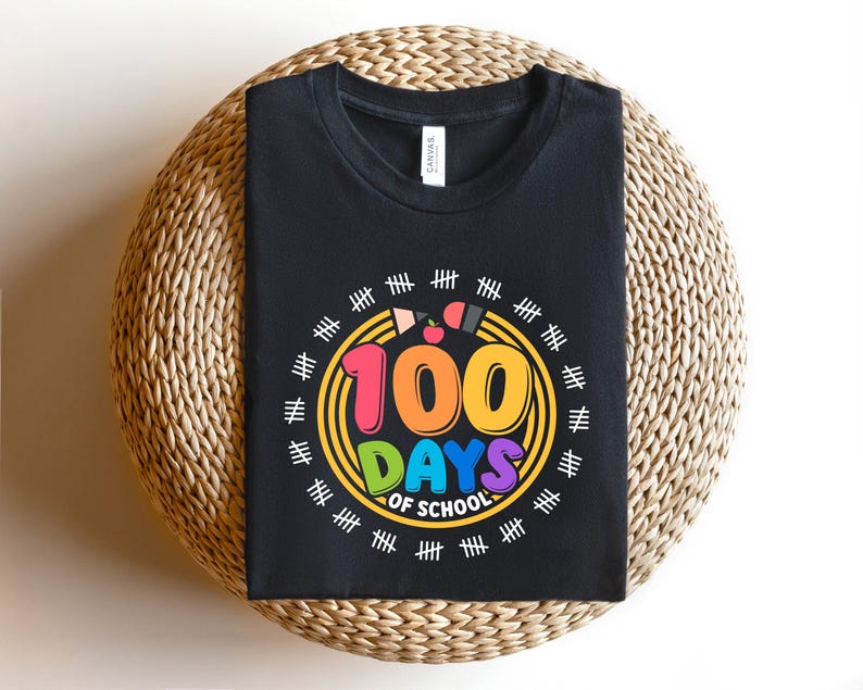 May include: Black t-shirt with a colorful graphic celebrating 100 days of school. The design features the text "100 DAYS OF SCHOOL" in vibrant colors, surrounded by a circle with pencils and tally marks. The shirt is displayed on a woven surface.