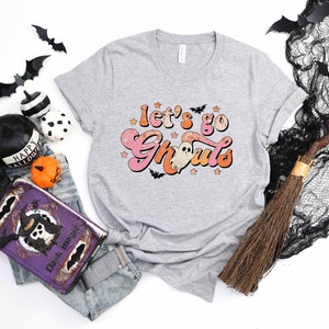May include: A gray t-shirt with a pink and orange graphic that says "Let's go Ghoul's" with a ghost and stars.