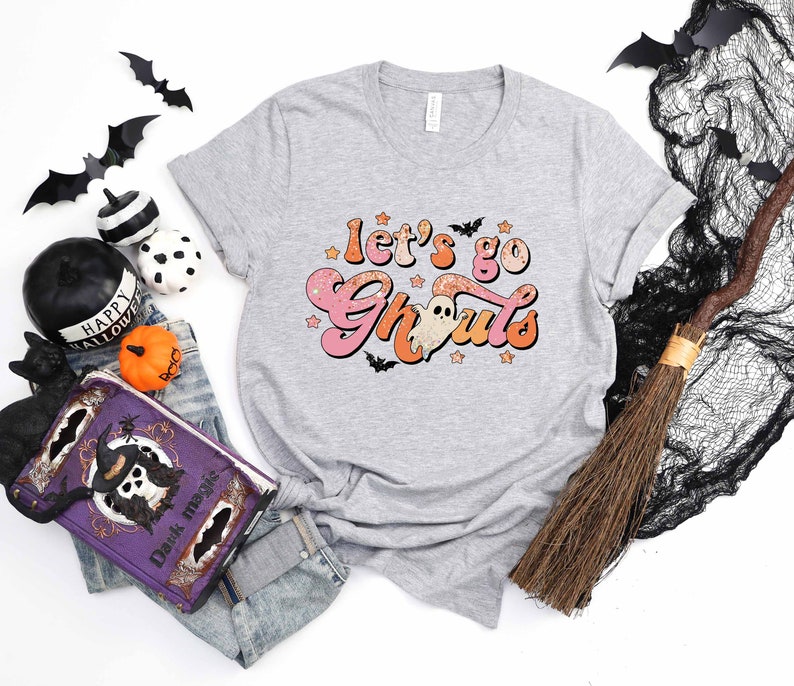 May include: A gray t-shirt with a pink and orange graphic that says "Let's go Ghoul's" with a ghost and stars.