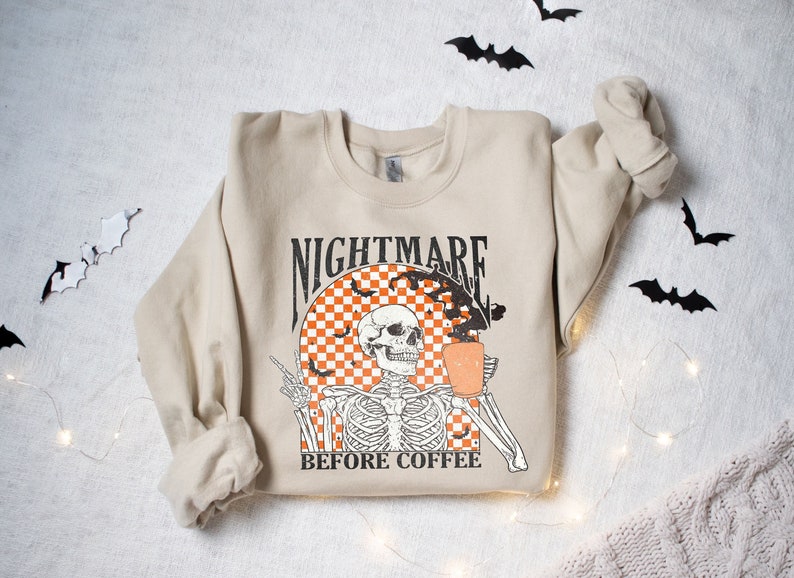 May include: A beige sweatshirt with a graphic print of a skeleton holding a cup of coffee. The graphic says "Nightmare Before Coffee".