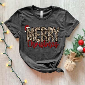 May include: A dark gray t-shirt with a leopard print "Merry Christmas" design. The word "Merry" is in a leopard print with a red Santa hat on top of the "M". The word "Christmas" is in red.