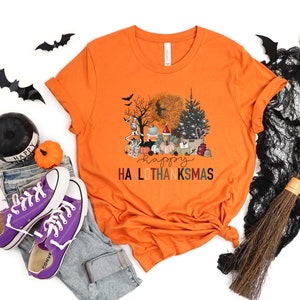 Puede incluir: Camiseta naranja con un gr&aacute;fico de una escena espeluznante de Halloween y Acci&oacute;n de Gracias con el texto "Happy Ha Lo Thanksmas".