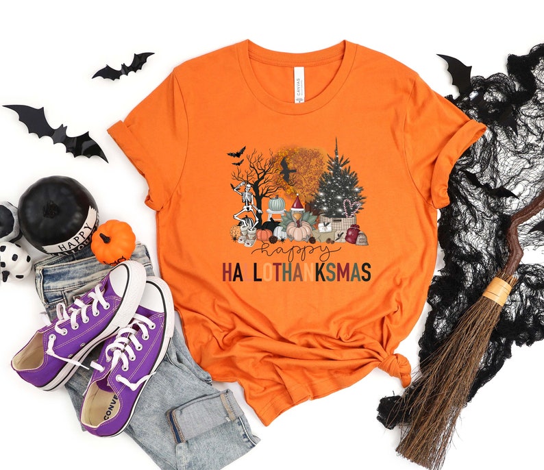 Puede incluir: Camiseta naranja con un gr&aacute;fico de una escena espeluznante de Halloween y Acci&oacute;n de Gracias con el texto "Happy Ha Lo Thanksmas".