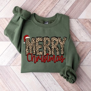 May include: A green sweatshirt with a leopard print "Merry Christmas" design. The word "Merry" has a red Santa hat on top.