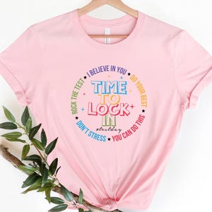 Könnte beinhalten: Hellrosa T-Shirt mit einem farbenfrohen kreisförmigen Design. Das Design enthält die Worte "TIME TO LOCK IN" und Sätze wie "I BELIEVE IN YOU" und "YOU CAN DO THIS", perfekt für den Testtag.