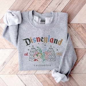 May include: Gray sweatshirt with a vintage-style Disneyland logo featuring a Christmas tree with Mickey Mouse and friends. The text reads "Disneyland est. 1955 California".