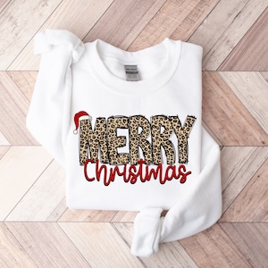 May include: White sweatshirt with a leopard print "Merry Christmas" design. The word "Merry" has a red Santa hat on top.
