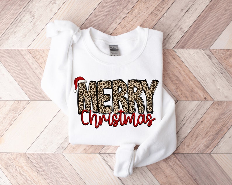 May include: White sweatshirt with a leopard print "Merry Christmas" design. The word "Merry" has a red Santa hat on top.