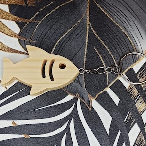 Peut inclure: Un porte-clés en bois en forme de poisson avec un design simple. Le poisson est brun clair et possède un anneau de clé.
