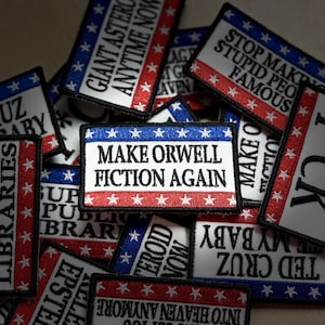 May include: A collection of rectangular embroidered patches featuring a white background with red and blue borders decorated with white stars. The patches display various black text slogans including Make Orwell Fiction Again and Support Public Libraries.