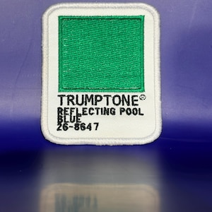 May include: A rectangular embroidered patch with a white border and a bright green square center. The text reads TRUMPTONE REFLECTING POOL BLUE 26-8647 in black lettering. The patch has rounded corners and a clean, stitched edge finish.