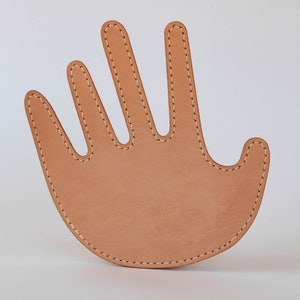 May include: A tan leather hand-shaped trivet with stitched edges.