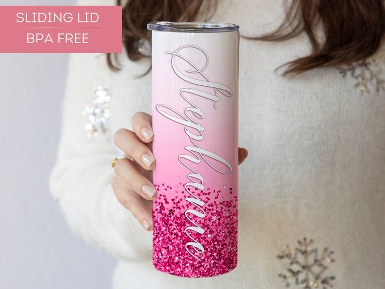 May include: A pink and white ombre stainless steel tumbler with a pink glitter design and the name "Stephanie" written in white cursive. The tumbler has a sliding lid and is BPA free.