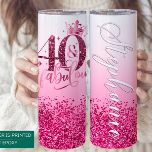 May include: Two pink and white stainless steel tumblers with a glitter design. One tumbler has the text "40 & fabulous" with a crown on top. The other tumbler has the name "Stephanie" written on it.