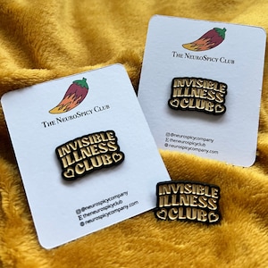 May include: Three black and gold enamel pins with the text "INVISIBLE ILLNESS CLUB" and heart accents, presented on white cards. The cards feature a chili pepper logo and the text "The NeuroSpicy Club". Social media handles are also visible.