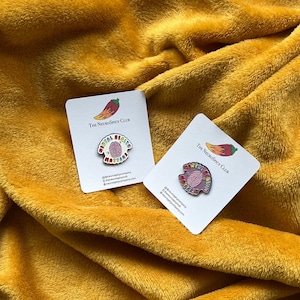 Puede incluir: Dos pines de esmalte sobre tarjetas blancas con el texto "Mental Health Matters" y un gráfico de cerebro. Las tarjetas también presentan el texto "The NeuroSpicy Club" y nombres de usuario de redes sociales. Los pines descansan sobre una superficie amarilla texturizada.