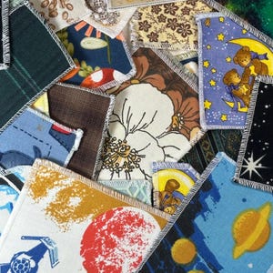 Peut inclure: Une collection de carrés de tissu assortis avec des bords blancs surjetés, présentant divers motifs imprimés incluant des thèmes spatiaux avec planètes et fusées, des motifs floraux, des oursons sur la lune et des formes géométriques variées.