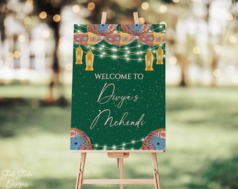May include: A green welcome sign with white text that reads "Welcome to Divya's Mehendi". The sign is decorated with colorful lanterns, string lights, and patterned designs.