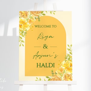 May include: A yellow and white welcome sign with floral accents. The sign reads "Welcome to Riya & Arjun's Haldi".