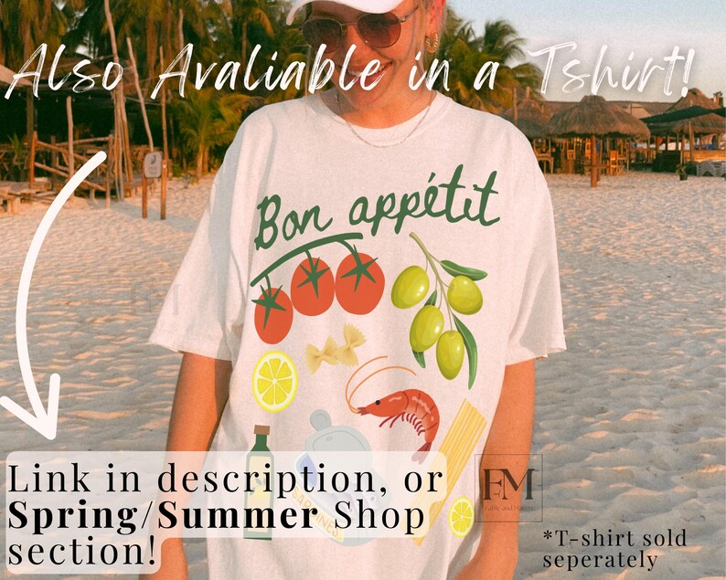 May include: White t-shirt with the text "Bon app&eacute;tit" in black lettering. The shirt features a graphic design of tomatoes, olives, pasta, a shrimp, and a lemon. The text "*T-shirt sold separately" is visible in the bottom right corner.