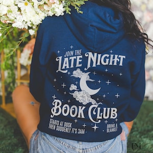 May include: A navy blue hoodie with a white graphic design that says "Join the Late Night Book Club". The graphic also includes a crescent moon, clouds, and stars. The text below the graphic says "Starts at dusk then suddenly it's 3am" and "Bring a blanket".
