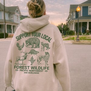 May include: A beige hoodie with a green graphic print of animals and the text "Support Your Local Forest Wildlife Pacific Northwest and Worldwide".
