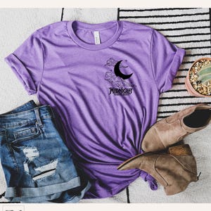 May include: A purple heather t-shirt with a black crescent moon and clouds graphic. The graphic also includes the text "Midnight Reading Society".