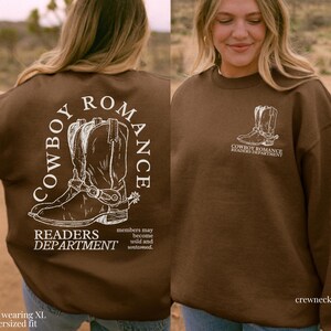 May include: Brown crewneck sweatshirt with a white graphic of cowboy boots and the text "Cowboy Romance Readers Department". The text "members may become wild and untamed" is also included on the sweatshirt.
