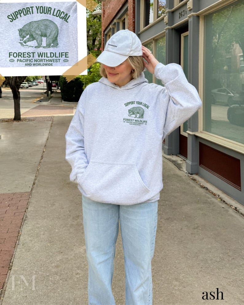 Puede incluir: Una sudadera con capucha gris con un gr&aacute;fico de oso verde y el texto "Support Your Local Forest Wildlife Pacific Northwest and Worldwide".
