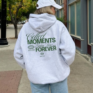 May include: A gray hooded sweatshirt with a green graphic print that says "Collect Moments Enjoy Now and Forever" with a globe and camera icon. The text "Since 1816" is below the graphic.