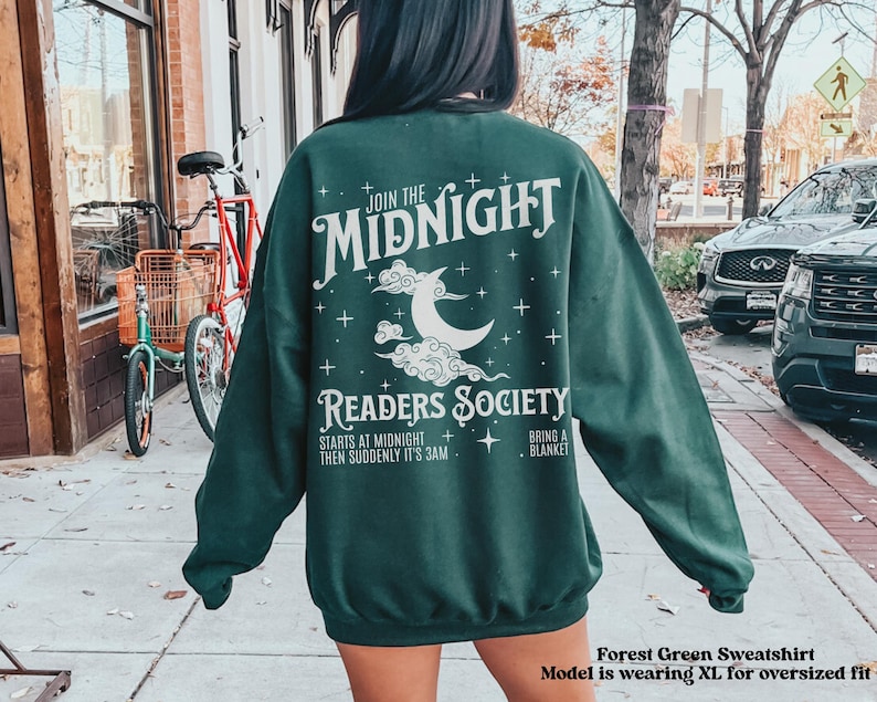 Może przedstawiać: Zielony sweatshirt z białym nadrukiem, na kt&oacute;rym widnieje napis "Join the Midnight Readers Society" z p&oacute;łksiężycem i gwiazdami. Tekst pod grafiką brzmi "Starts at midnight, then suddenly it's 3am. Bring a blanket."
