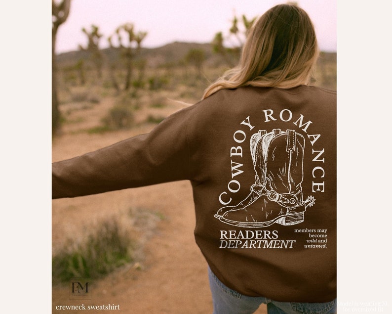May include: Brown crewneck sweatshirt with a white graphic of cowboy boots and the text "COWBOY ROMANCE" and "READERS DEPARTMENT". The text below the graphic reads "members may become wild and untamed."