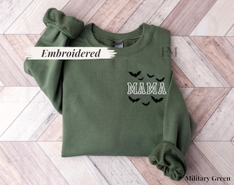 May include: Military green sweatshirt with the word "MAMA" in white block letters, surrounded by black bat silhouettes. The word "Embroidered" is written across the top left of the sweatshirt.